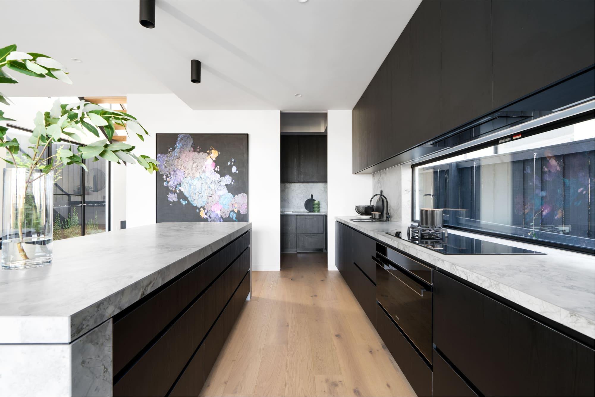 A modern kitchen with oak timber flooring, stone benches and discreet butlers kitchen