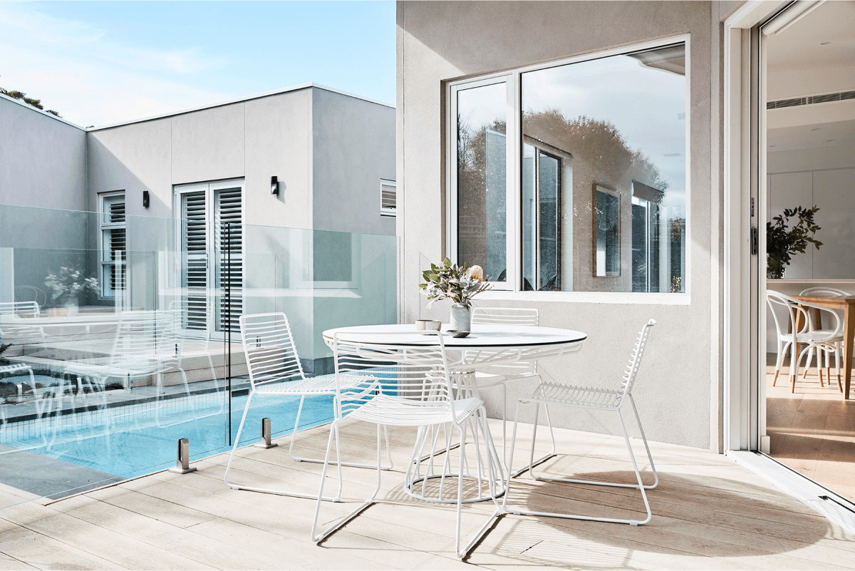 An exterior outdoor patio with a pool, featuring a white table and chairs.