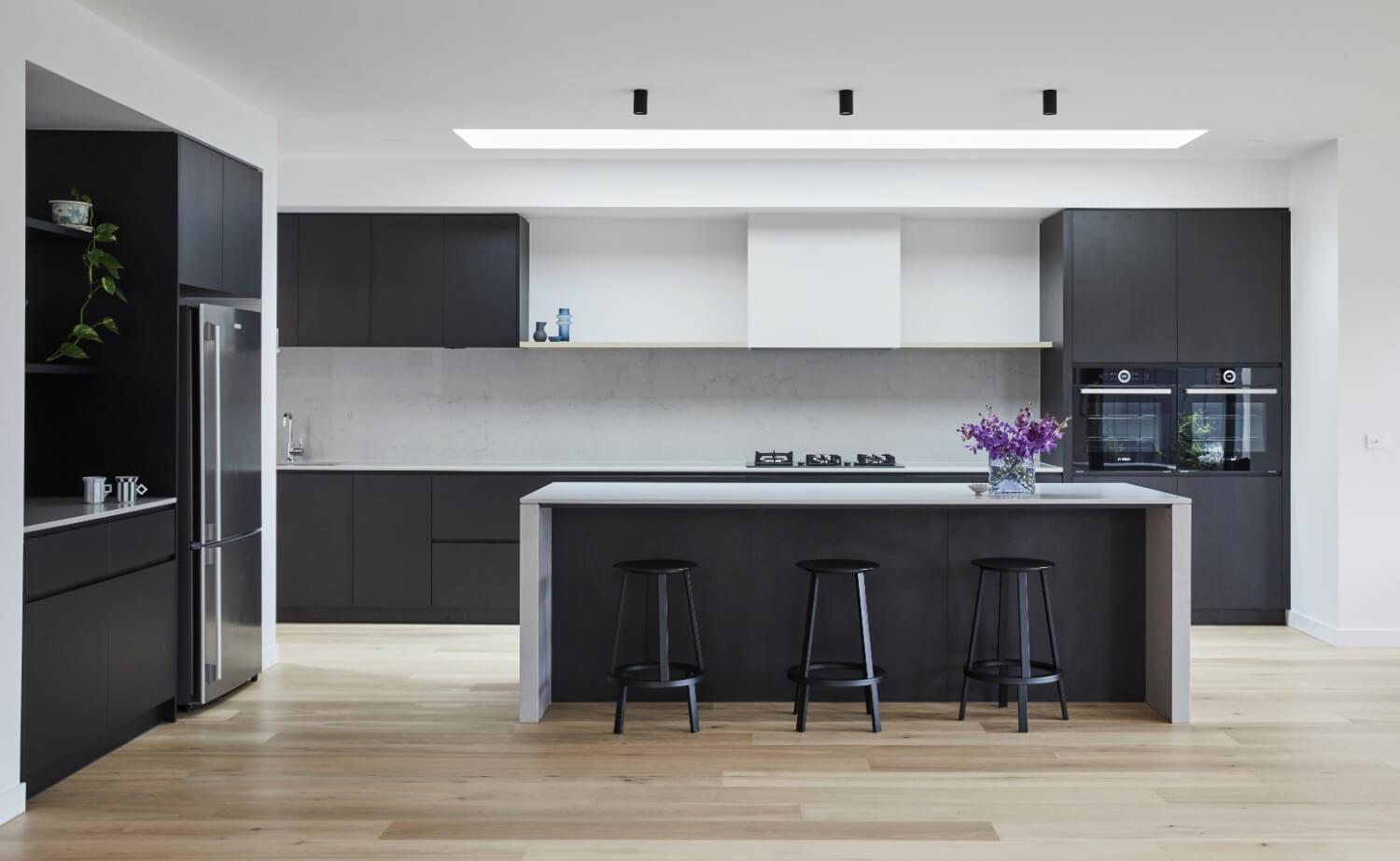 Black Cabinetry Contrasts Against Natural White Benchtops And Rangehood